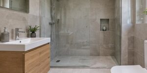 Compact bathroom with large pale stone-effect tiles, an oak vanity and a glass shower screen