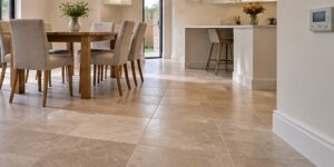 Sunlit kitchen and dining room with a continuous stone-effect tiled floor and a wall heating control